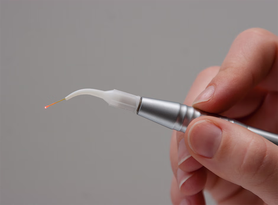 Hand holding a dental laser tool with a red light tip against a gray background.