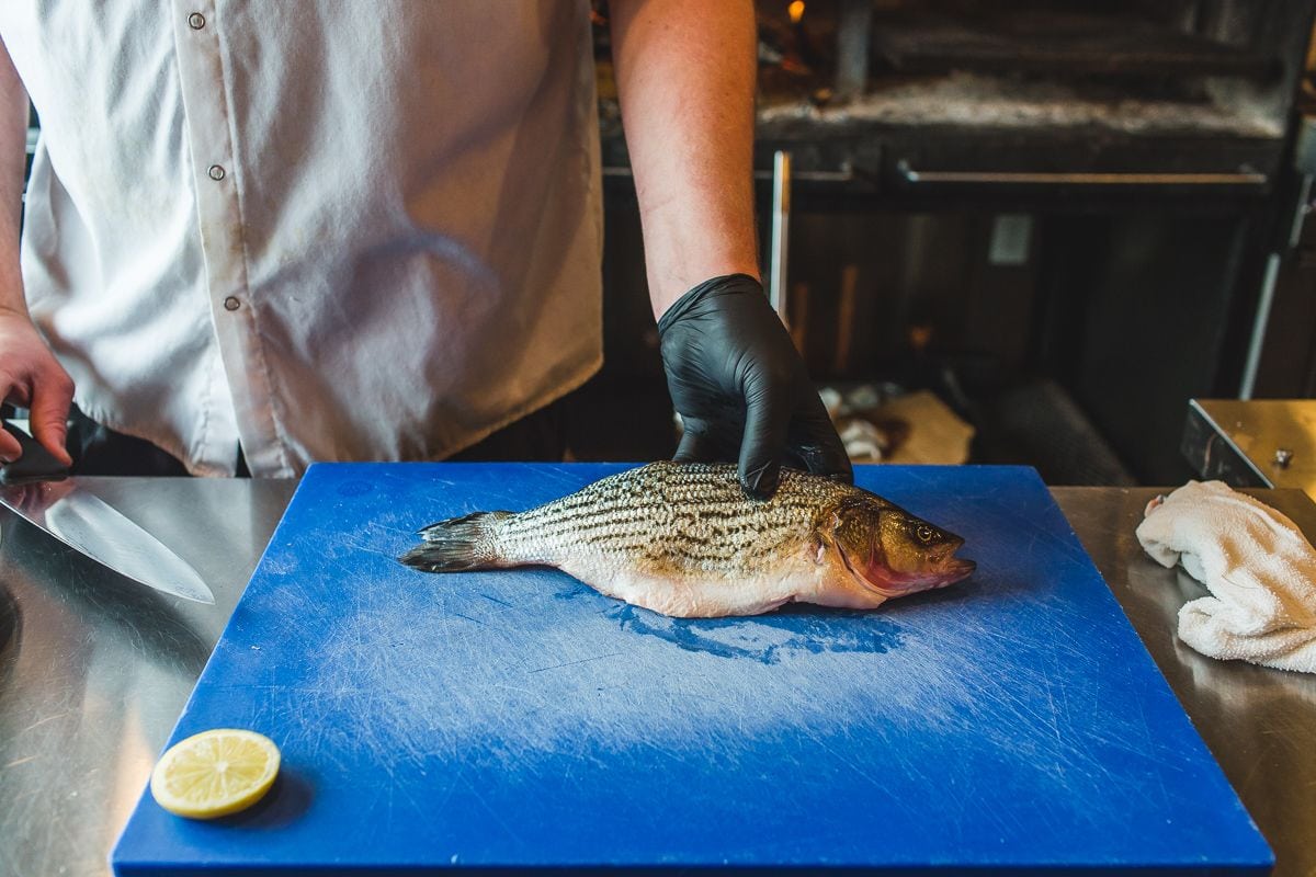 Person wearing gloves about to cut a fresh fish on a cutting board