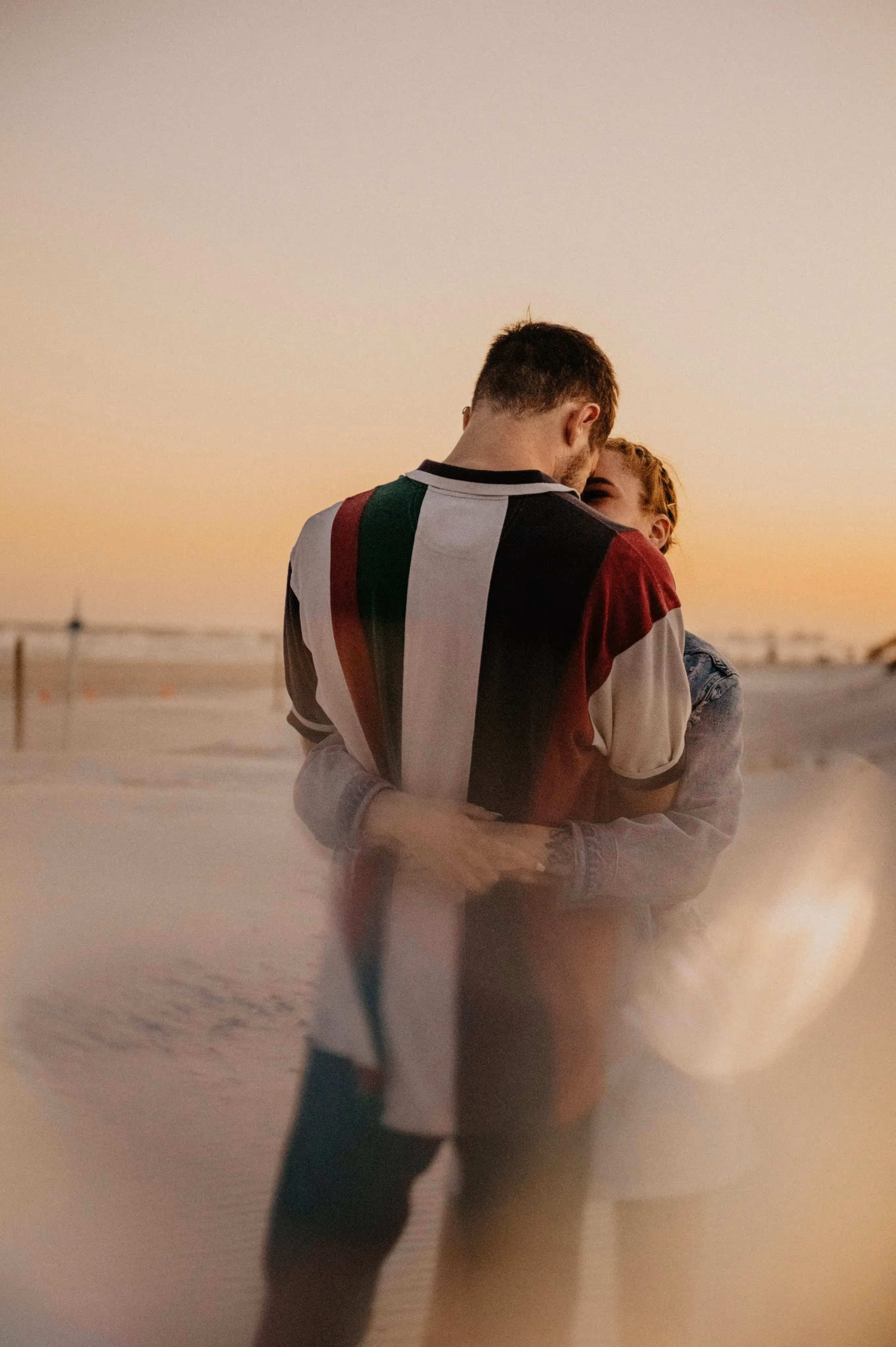 Couple embracing on a beach at sunset with soft, warm lighting.