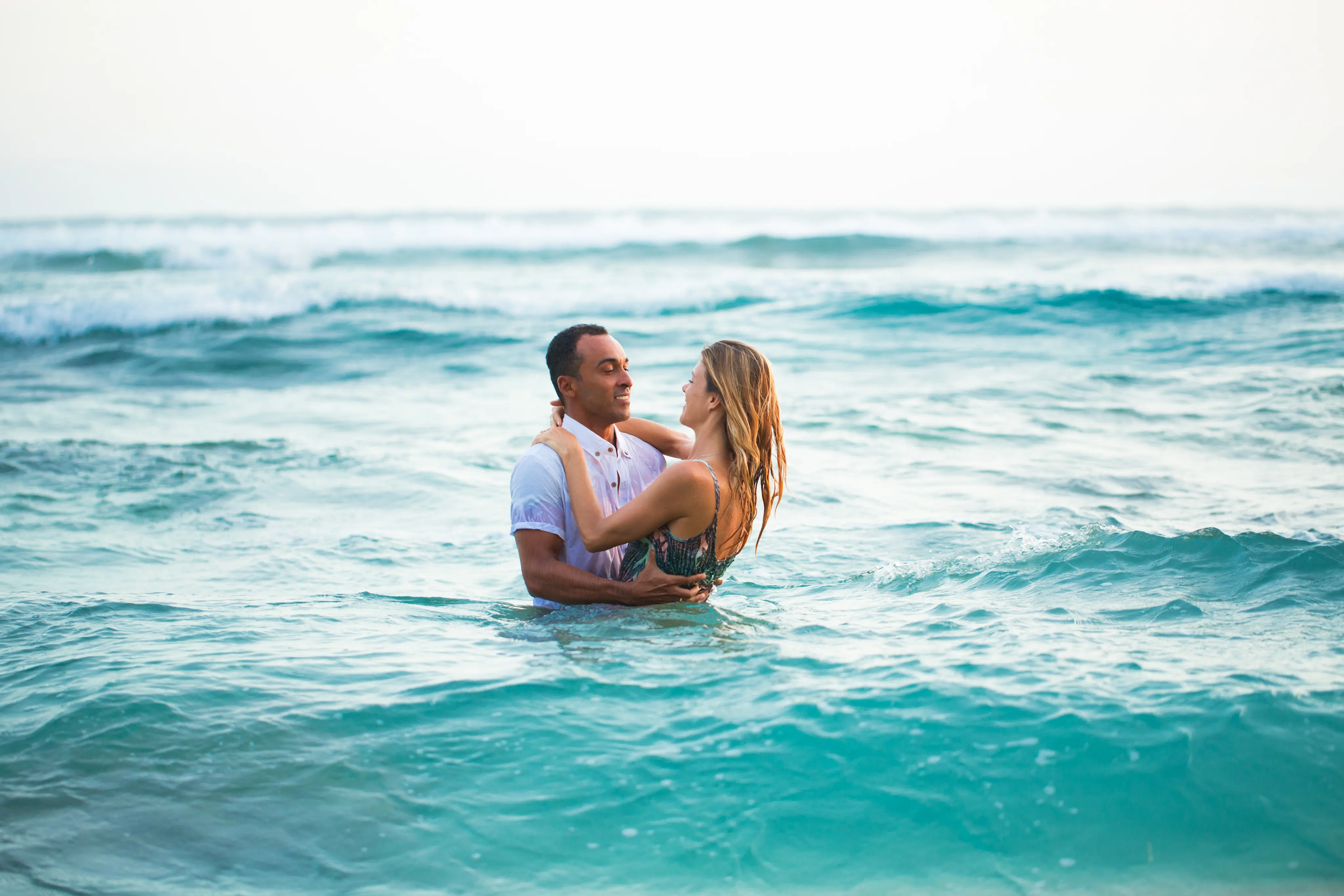 Couple embracing in the ocean with waves around them during daytime.