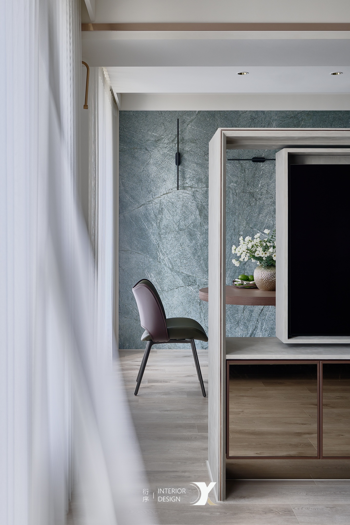 Modern interior with a chair facing a green textured wall, a wooden table with white flowers, and a TV unit with reflective panels.