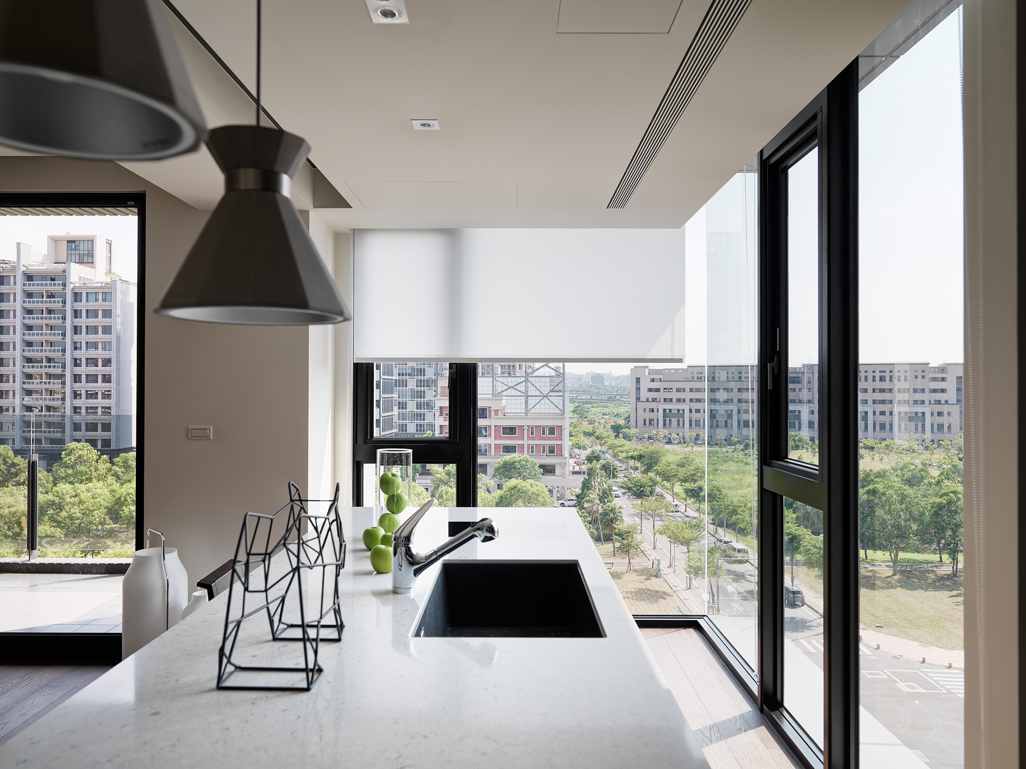 Minimalist living room with L-shaped gray sofa, glass coffee table, large windows with blinds, and modern art pieces.