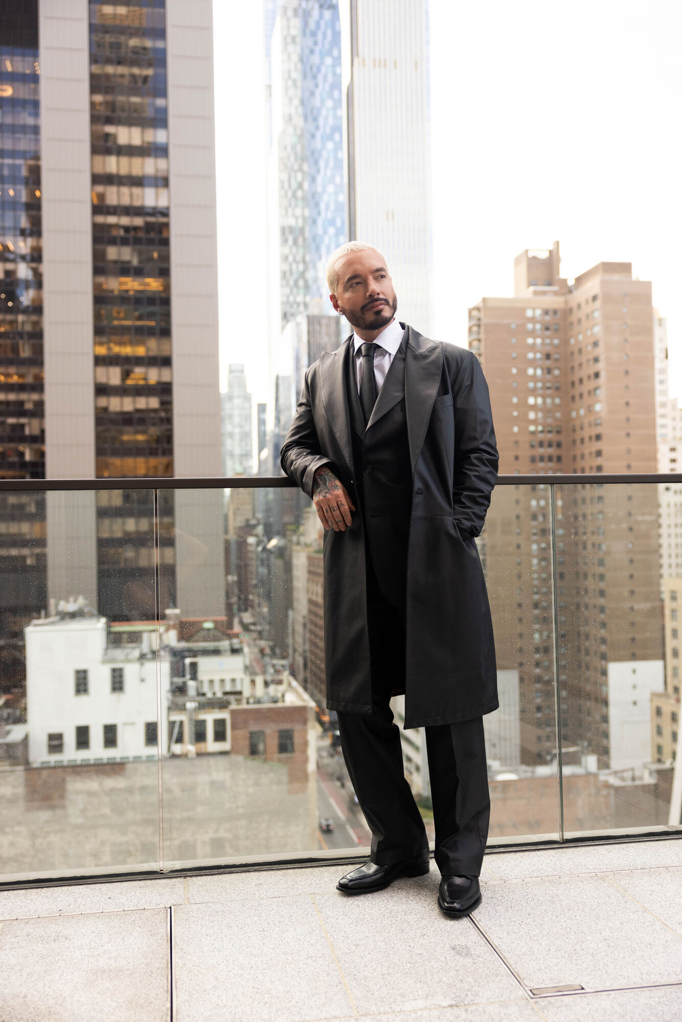 J Balvin in a long dark overcoat on a Manhattan rooftop terrace.