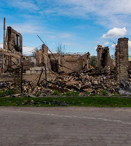 Verwoeste stenen gebouwen met ingestorte muren en puin onder een blauwe lucht met wolken.
