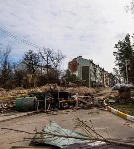Verwoeste straat met omgevallen bomen en puin voor beschadigde appartementen in een stedelijk gebied.