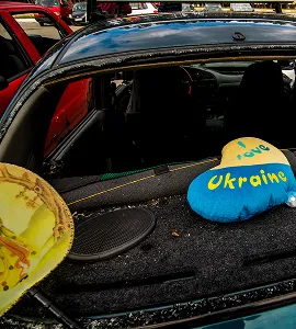 Hartvormig kussen met tekst 'Love Ukraine' liggend in de achterbak van een blauwe auto.