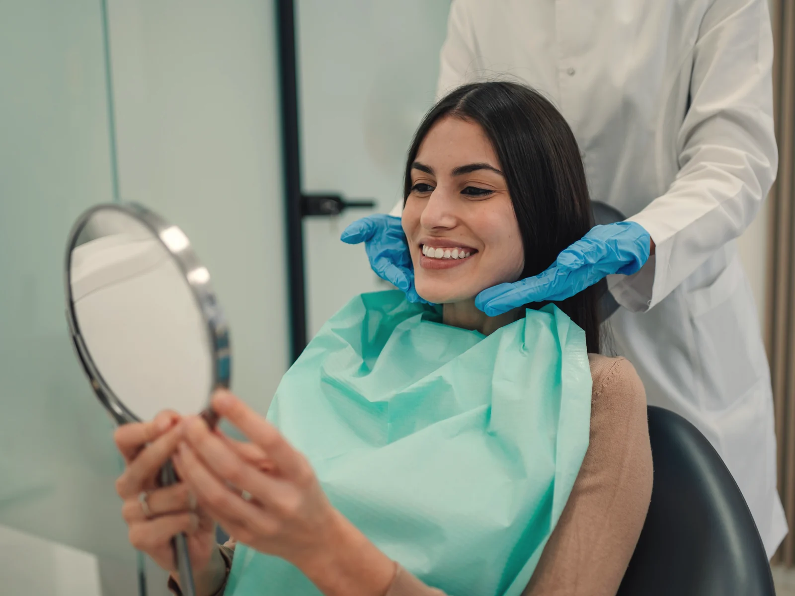 Paciente latina mirándose la sonrisa en un espejo en el sillón dental