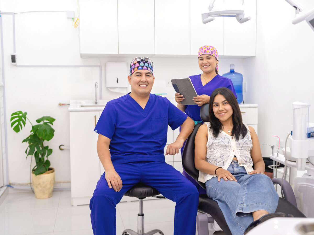 Equipo dental sonriente recibiendo a una paciente joven en el sillón en su primera cita