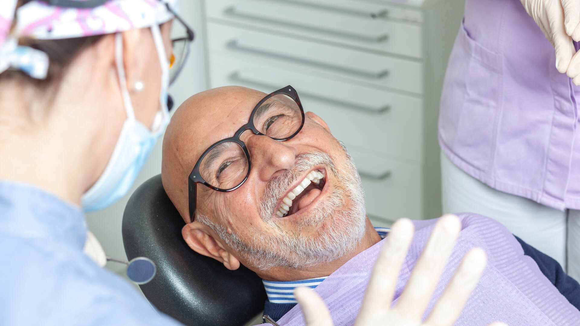 Paciente mayor riendo tranquilo en el sillón dental mientras la dentista le explica la revisión
