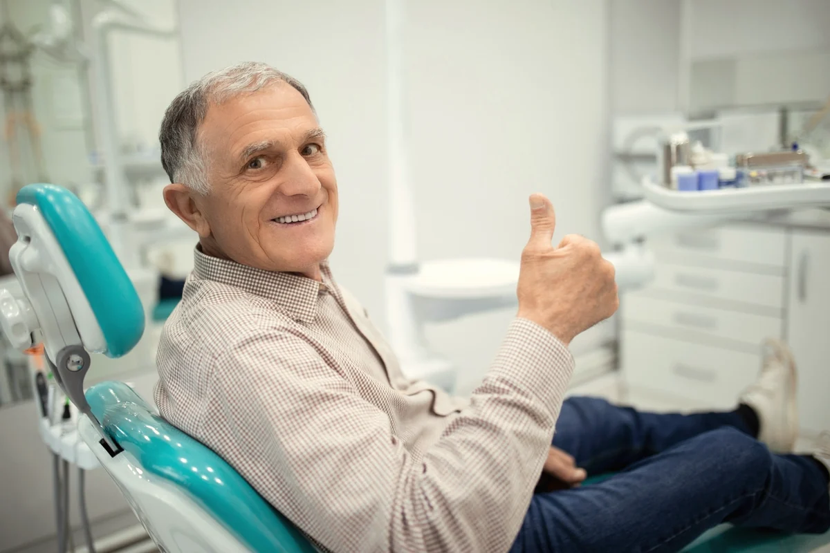 Hombre mayor latino sonriendo en el sillón dental tras su revisión