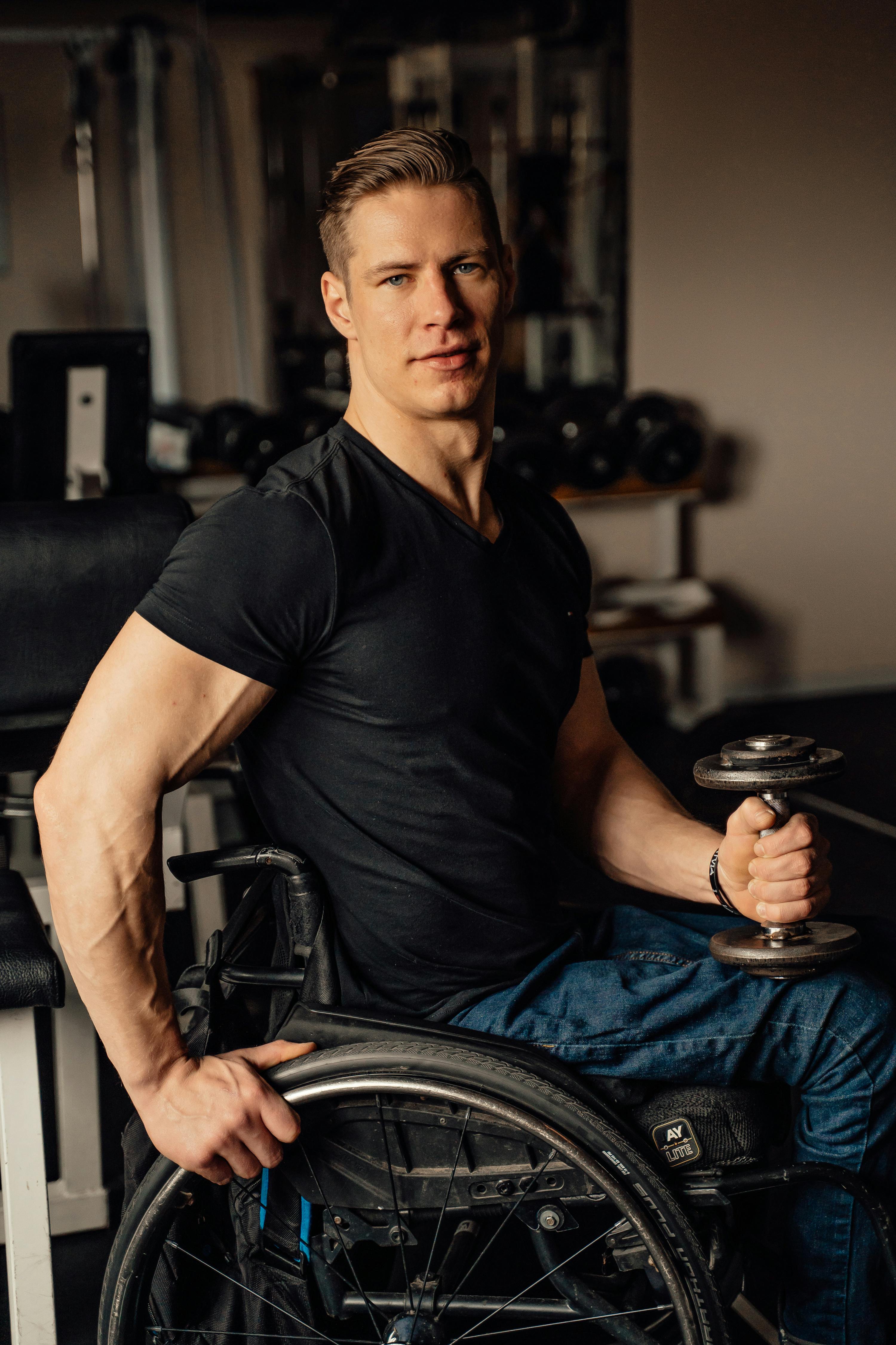 Muscular man sitting in a wheelchair holding a dumbbell in a gym.