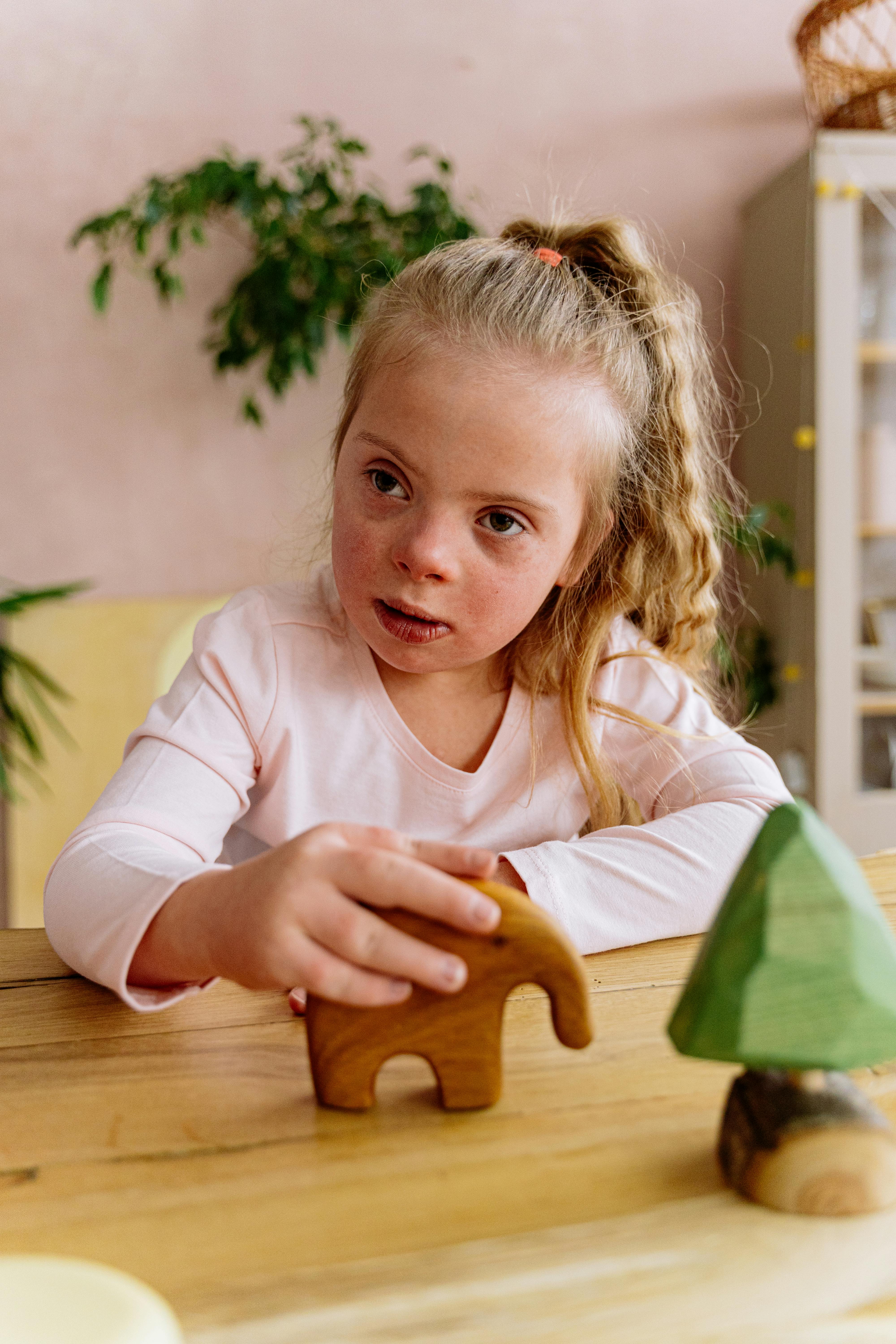 Young girl with Down syndrome playing with a wooden elephant toy at a table.