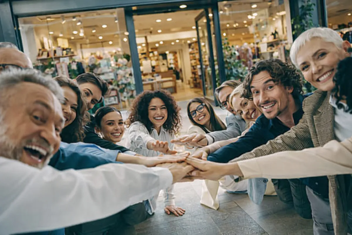 Un groupe de personnes souriantes mettant les mains ensemble en signe d'unité pour représenter la communauté "J'Ouvre Ma Boutique"