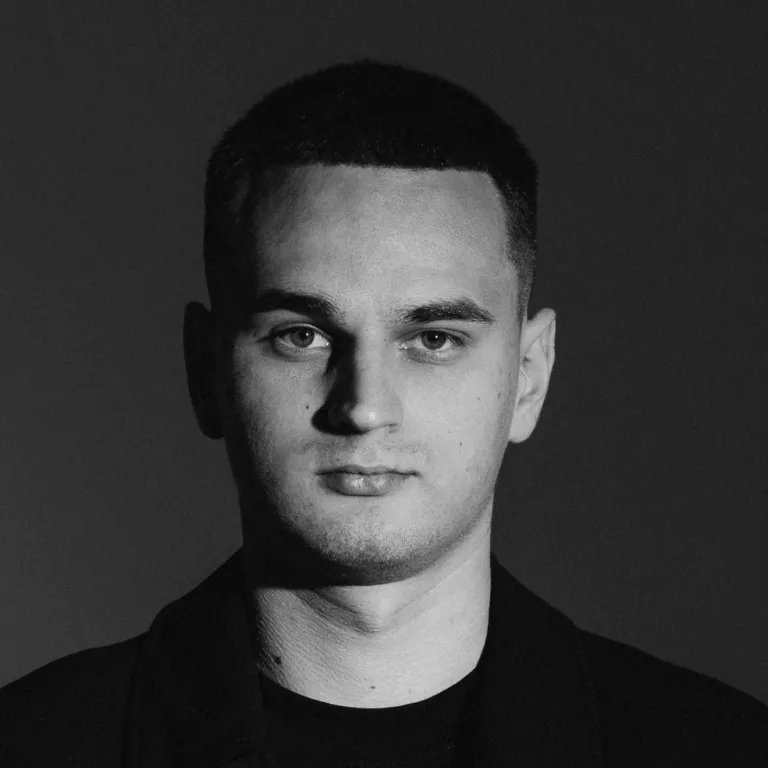 Black and white portrait of a young man with short hair and a neutral expression against a dark background.