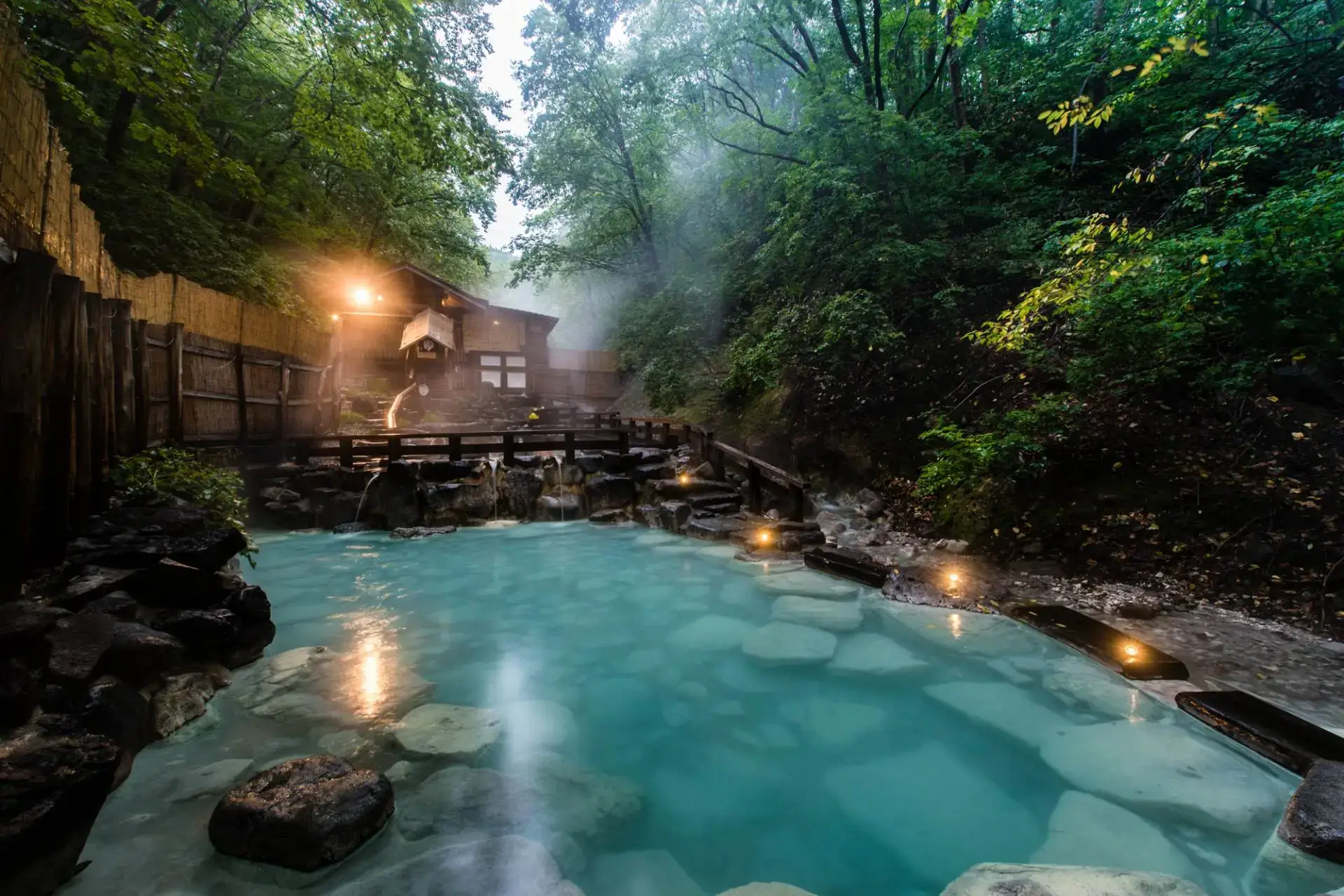 Outdoor Japanese onsen surrounded by wooden walls and stones in a forest, illustrating Japan's hot spring culture