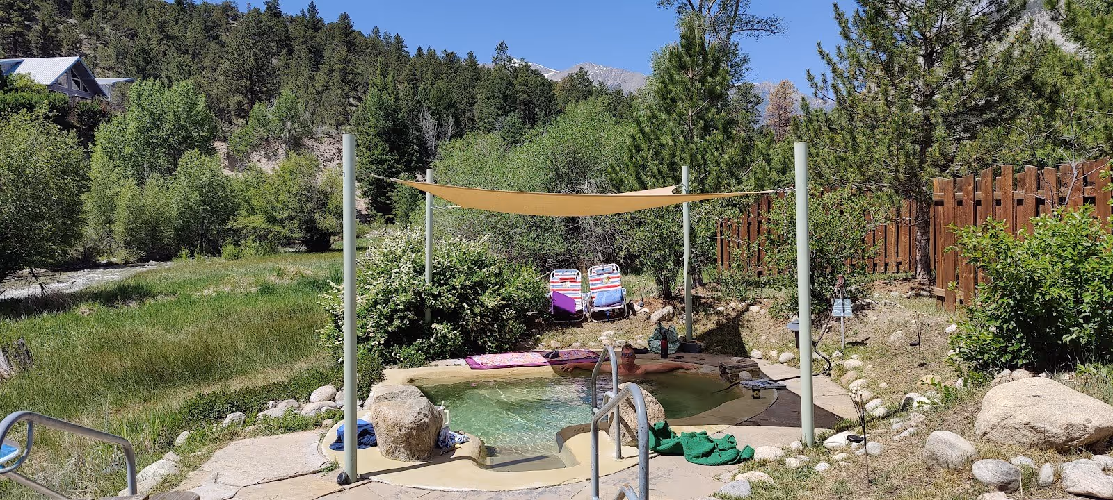 Person relaxing in shaded Antero Hot Springs Cabins outdoor pool with greenery and mountain view near Nathrop, Colorado