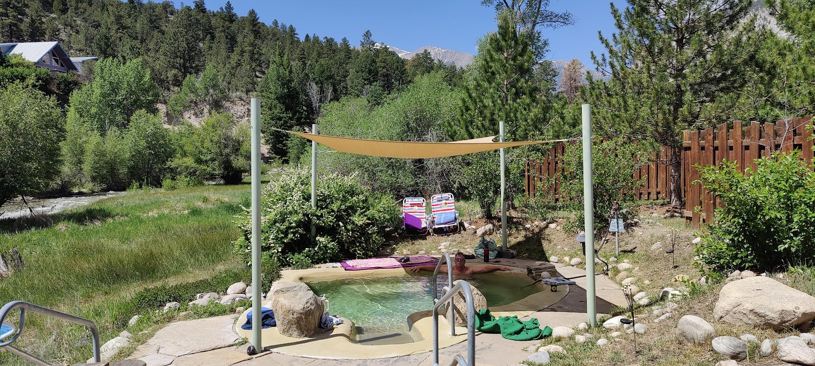 Person relaxing in shaded Antero Hot Springs Cabins outdoor pool with greenery and mountain view near Nathrop, Colorado