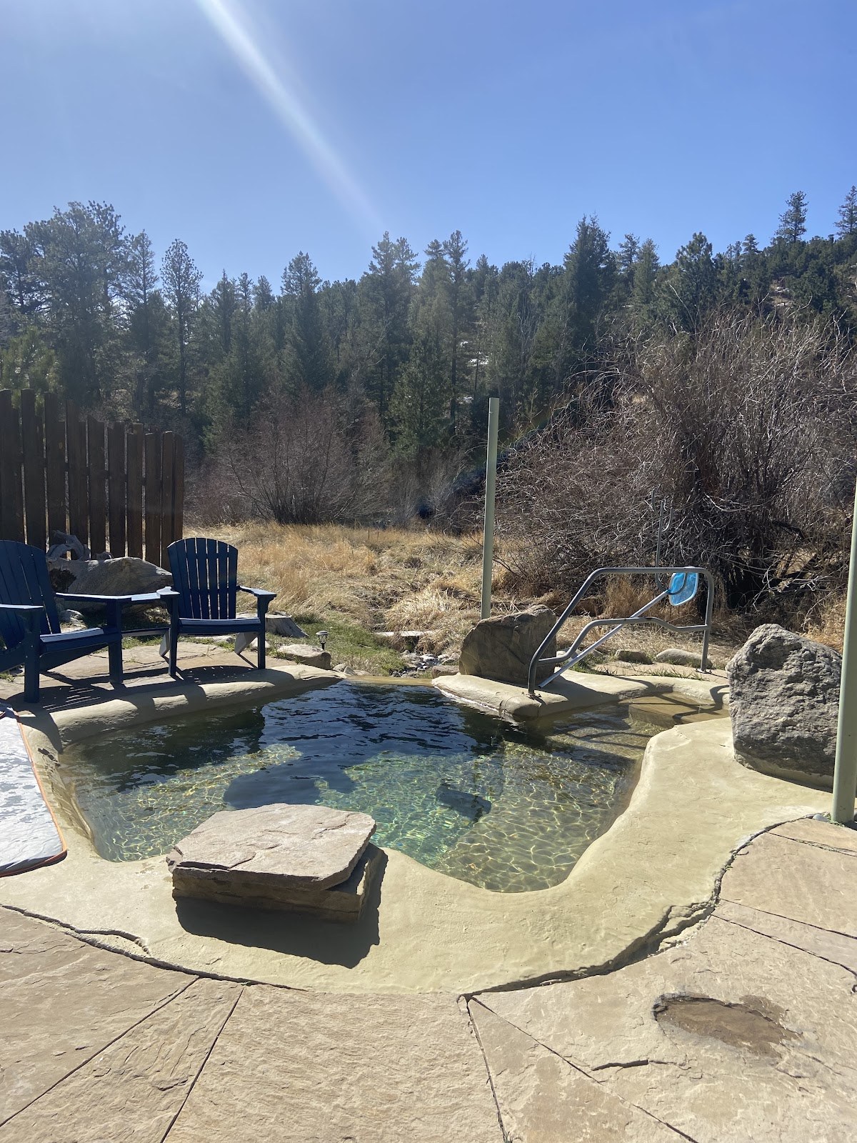 Outdoor Antero Hot Springs Cabins pool with clear water surrounded by natural stone and Adirondack chairs in Nathrop, Colorado