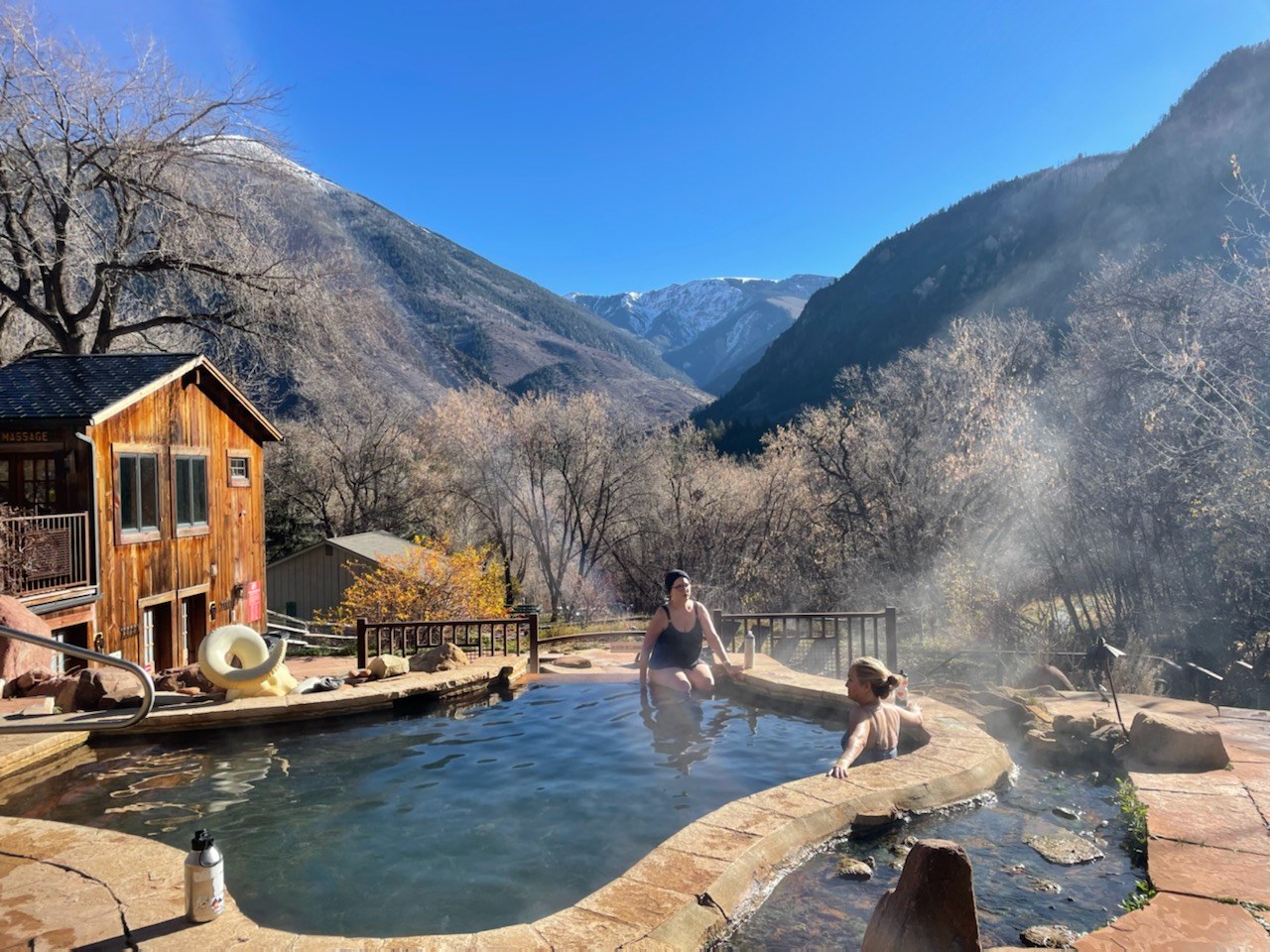 Two women enjoy the steamy outdoor spa pool at Avalanche Ranch Cabins & Hot Springs near Redstone, Colorado with mountain views.
