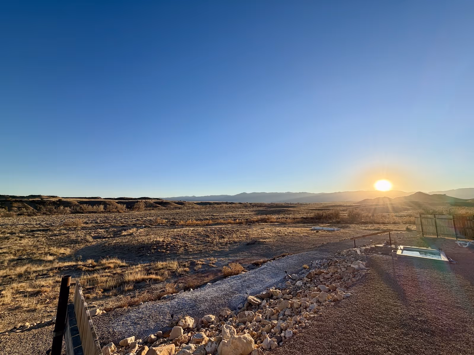 Wide view of Desert Reef Hot Springs with clear blue water pool at sunset near Florence, Colorado, showing arid terrain and distant mountains.