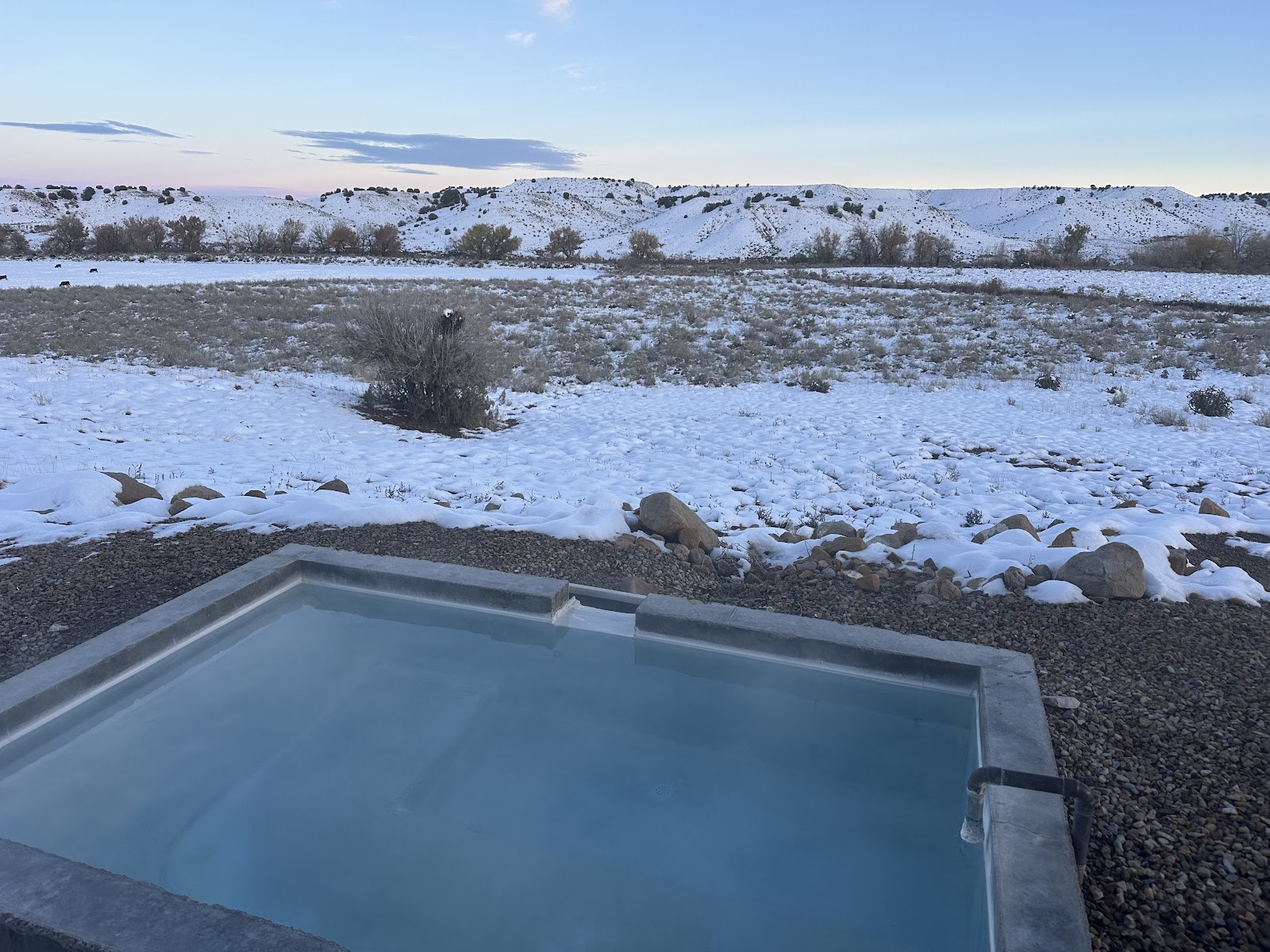 Desert Reef Hot Springs pool overlooking snow-covered plains and rocky hills near Florence, Colorado in the winter season under a calm sky.