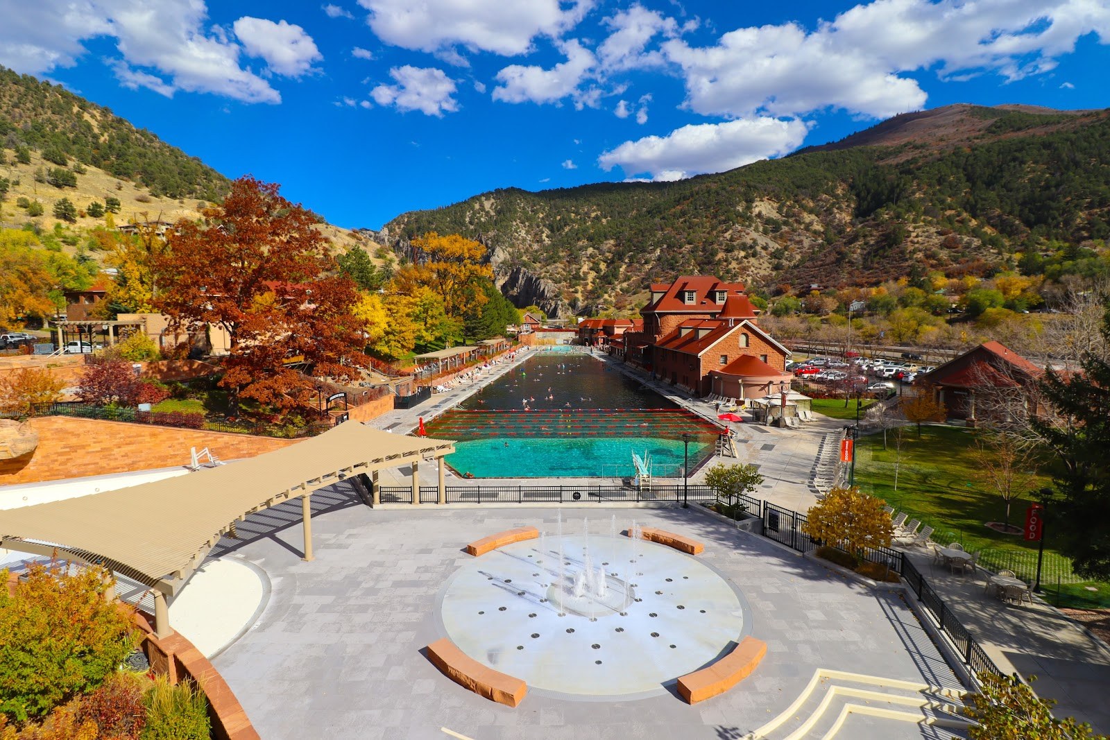 Sunny daytime view of Glenwood Springs outdoor spa pool area with colorful autumn trees and mountainous landscape near Aspen, Colorado.