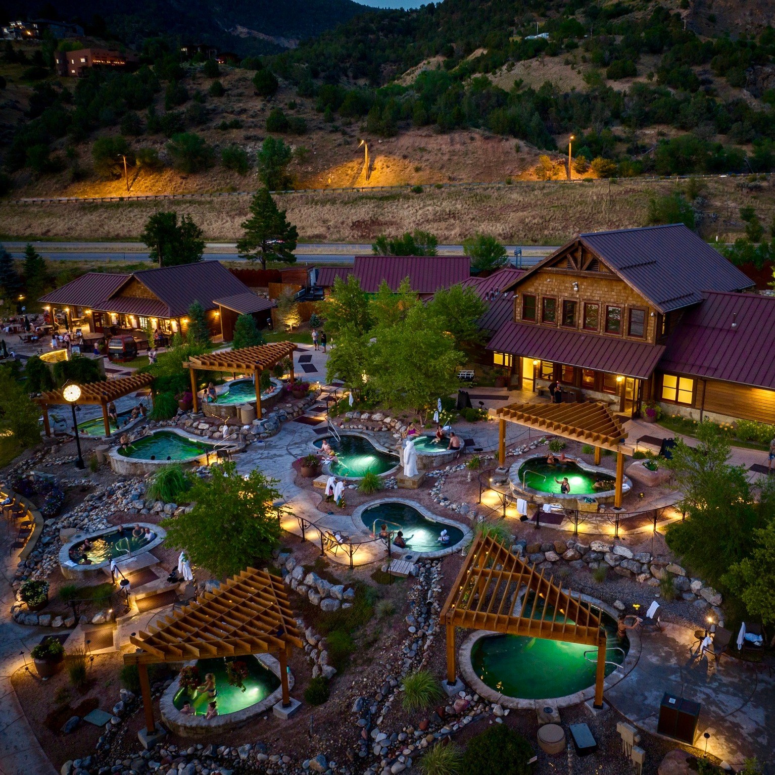 Night aerial view of illuminated hot spring pools at Iron Mountain Hot Springs in Glenwood Springs, Colorado with cozy seating and nearby buildings