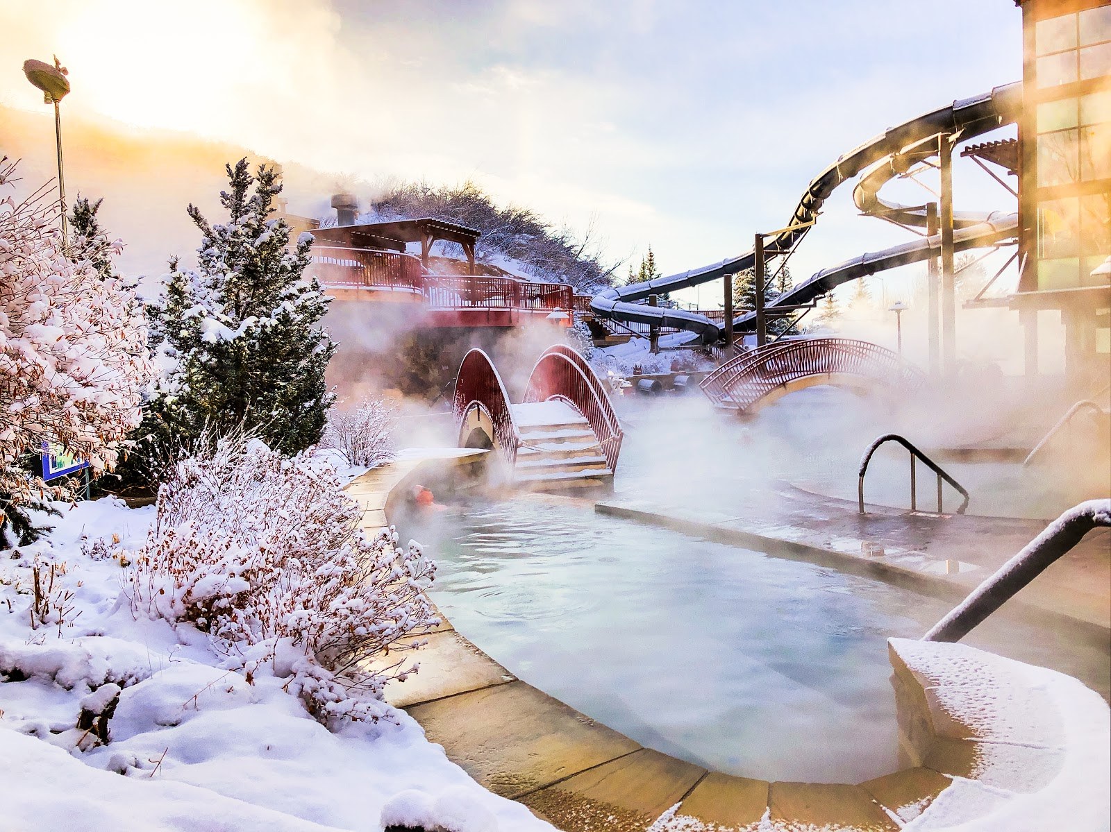 Steam rising from outdoor hot springs at Old Town Hot Springs in snowy Steamboat Springs, Colorado with bridges and water slides visible