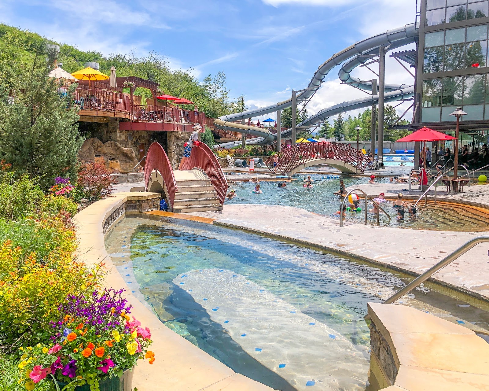 Outdoor pool area at Old Town Hot Springs in Steamboat Springs, Colorado with slides, bridges, and colorful umbrellas on a sunny day