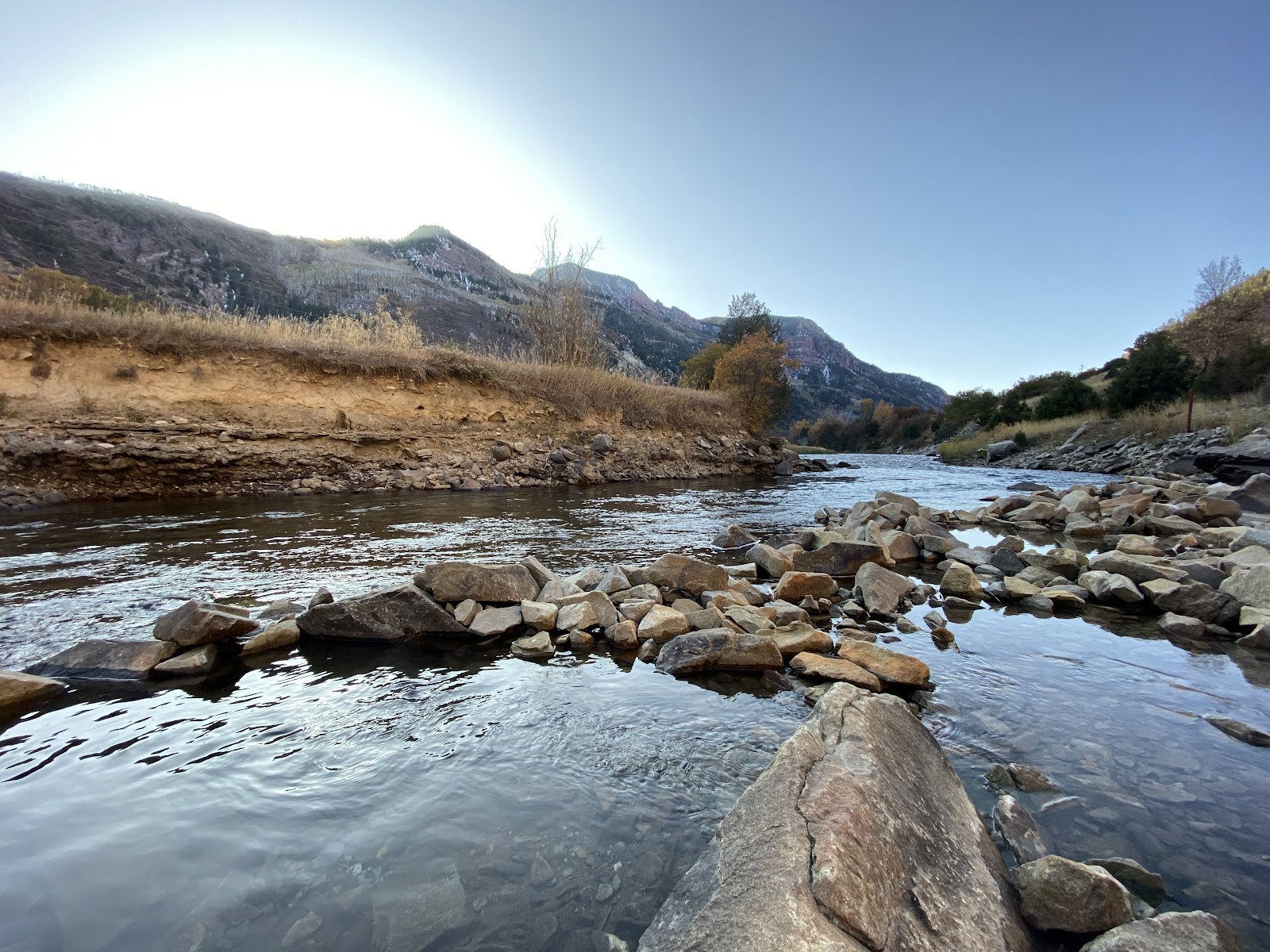 Clear water in natural hot spring pools formed by rocks next to a river with mountainous terrain near Redstone, Penny Hot Springs.