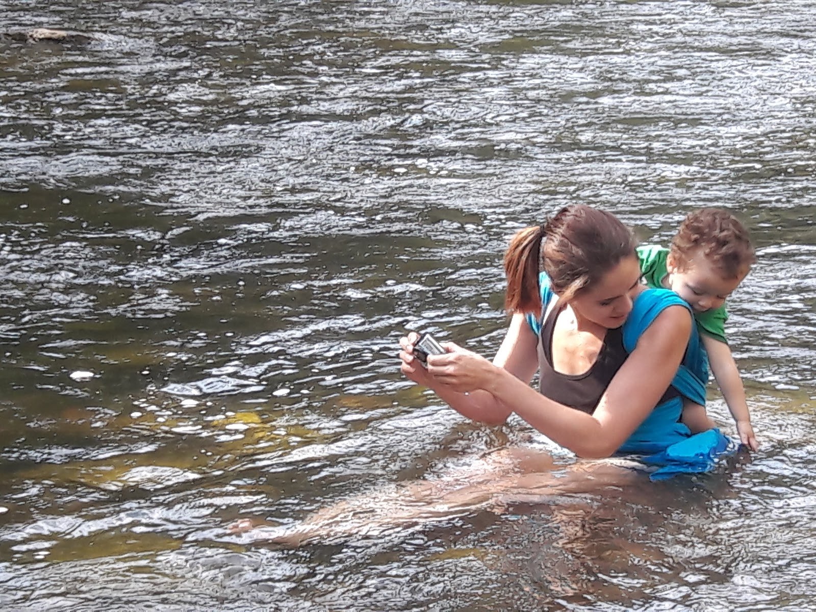 A woman with a child on her back sitting and relaxing in the Piedra River Hot Springs water near Pagosa Springs, Colorado, USA
