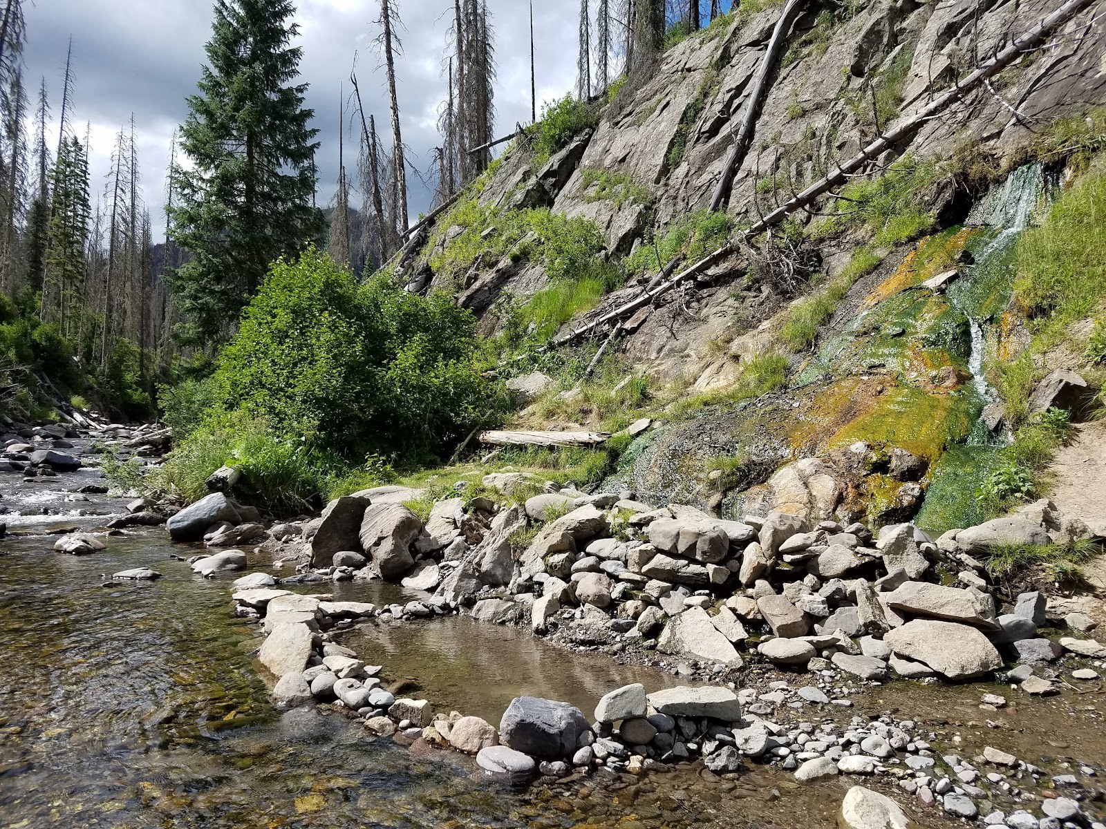 Natural hot spring pool bordered with rocks beside a riverbank at Rainbow Hot Springs near Pagosa Springs in Colorado, United States