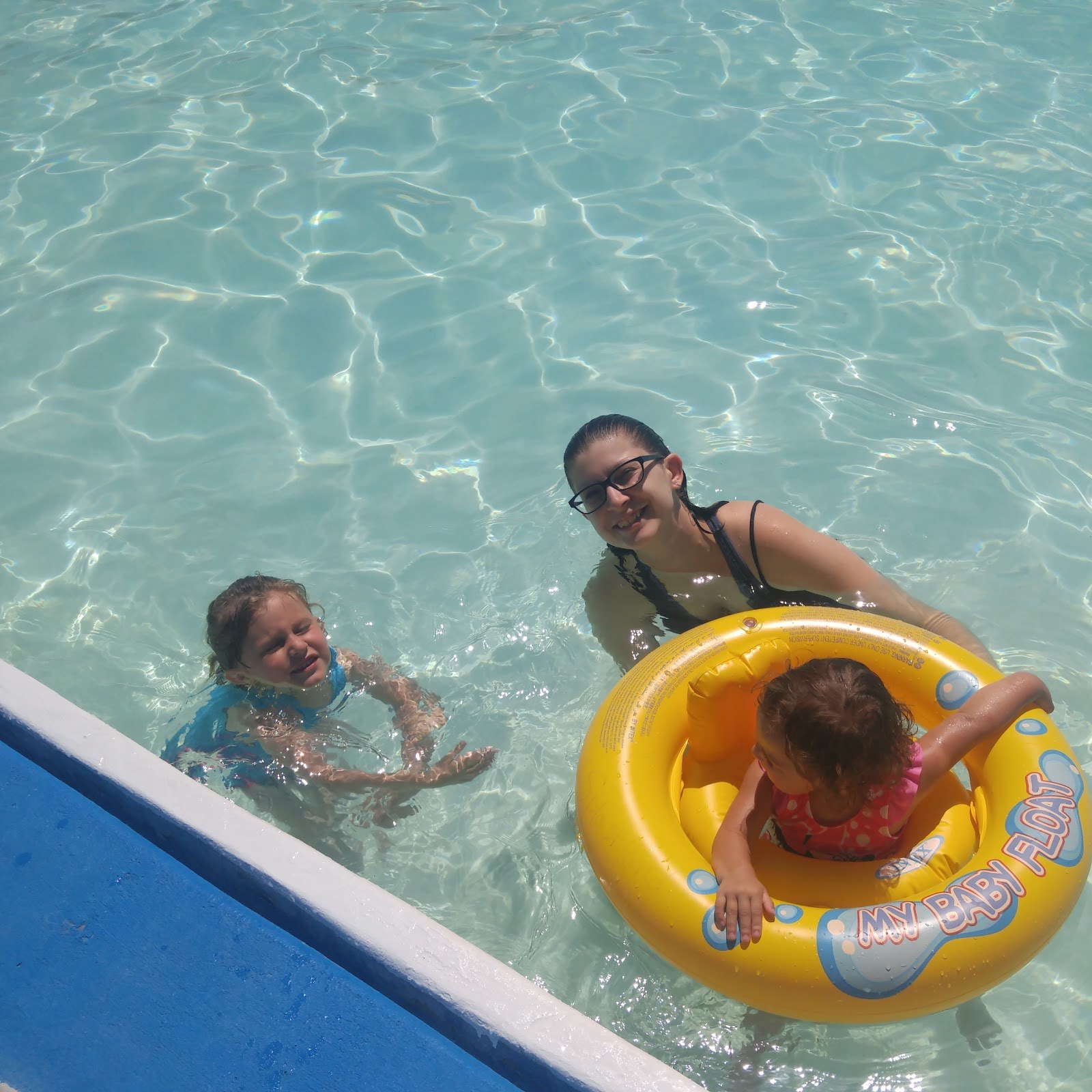 Three people enjoying the clear water at Splashland Hot Springs in Alamosa, Colorado, with a child in a yellow float ring.