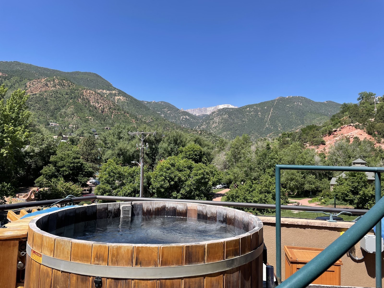 Wooden outdoor hot spring tub overlooking green mountains and clear blue sky at SunWater Spa Hot Springs near Manitou Springs, Colorado.