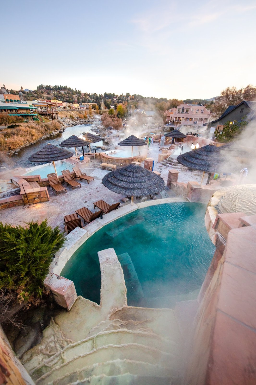 Steamy outdoor hot spring pools with thatched umbrellas and lounge chairs at The Springs Resort & Spa in Pagosa Springs, Colorado