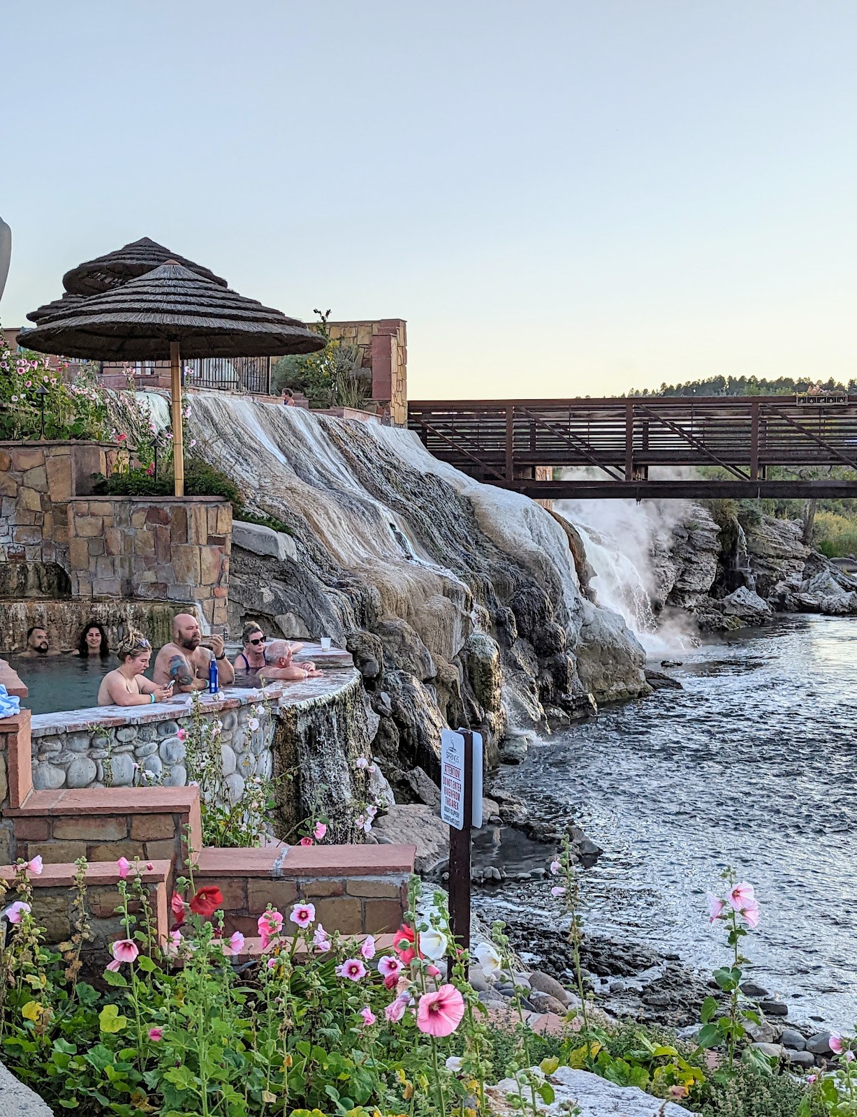 People relaxing in hot spring pool next to waterfall and flower garden at The Springs Resort & Spa in Pagosa Springs, Colorado