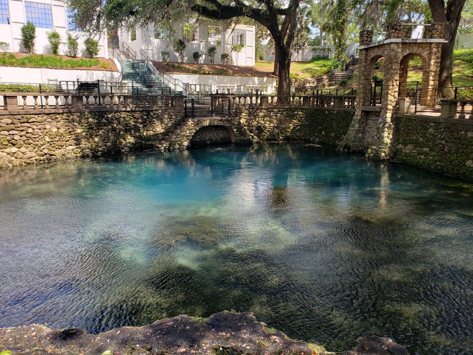 Stone-walled spring pool with classic architecture and white building in background at Radium Springs Gardens by Albany, Georgia, USA