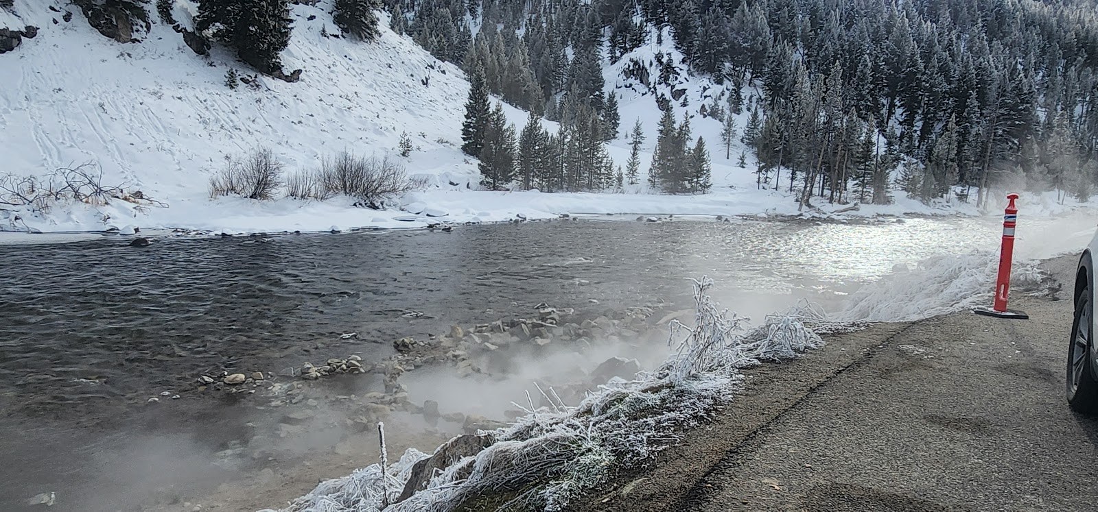 Steam rising from Boat Box Hot Spring beside a roadside near Stanley, Idaho, with snow-covered scenery and a vehicle nearby