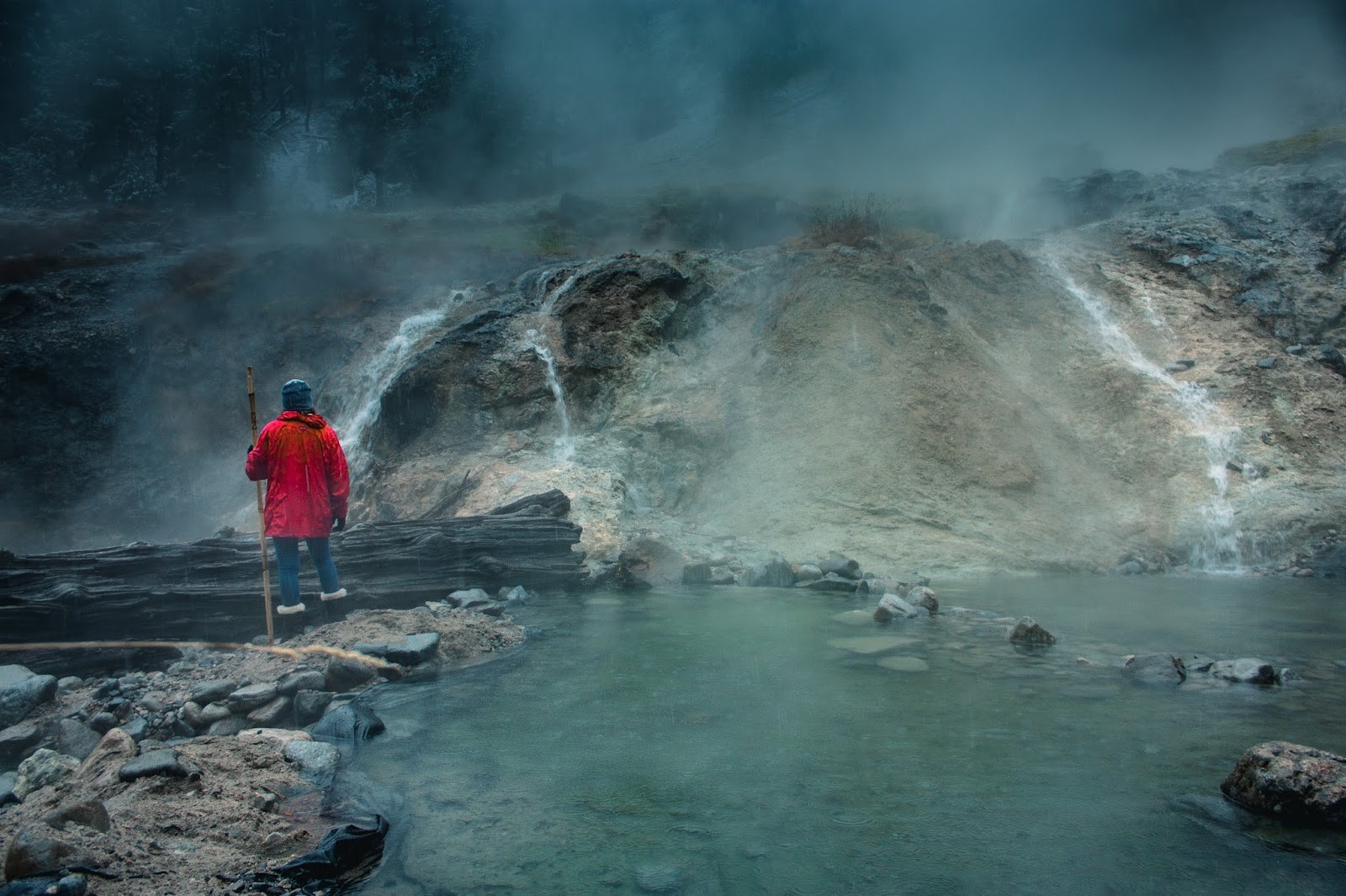 Person in red jacket standing by a steaming hot spring pool with small waterfalls at Bonneville Hot Springs near Lowman, Idaho