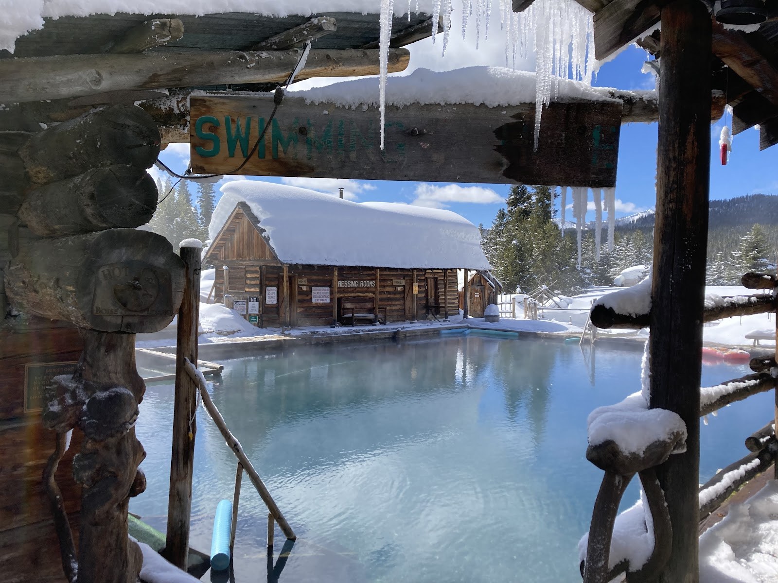 Winter scene of Burgdorf Hot Springs outdoor pool with snow-covered log cabins and icicles in McCall, Idaho, United States.