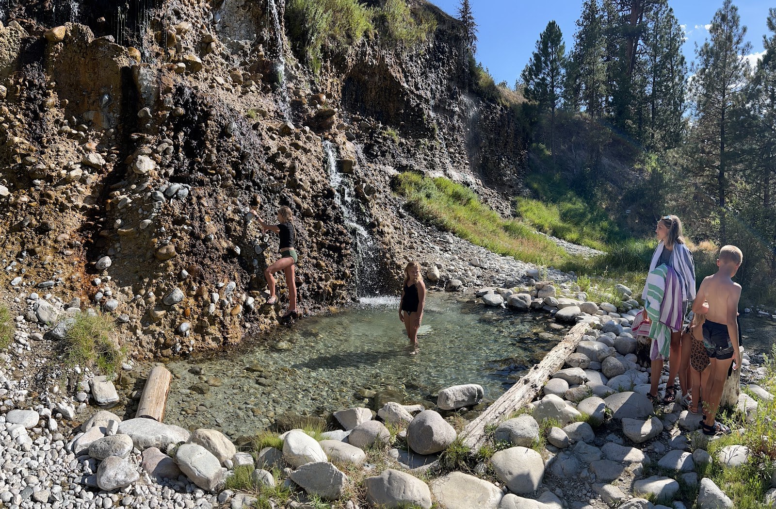 People soaking in a clear outdoor pool beside a rocky cliff with a small waterfall at Chattanooga Hot Springs near Atlanta, Idaho, US.
