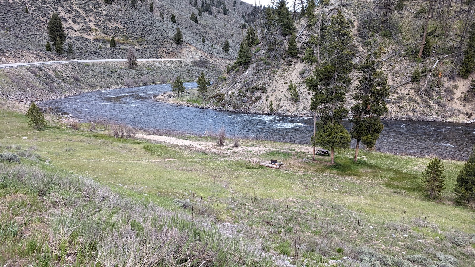 Scenic view of a river winding through a grassy meadow with trees and hills at Cove Creek Hot Springs near Stanley, Idaho, United States
