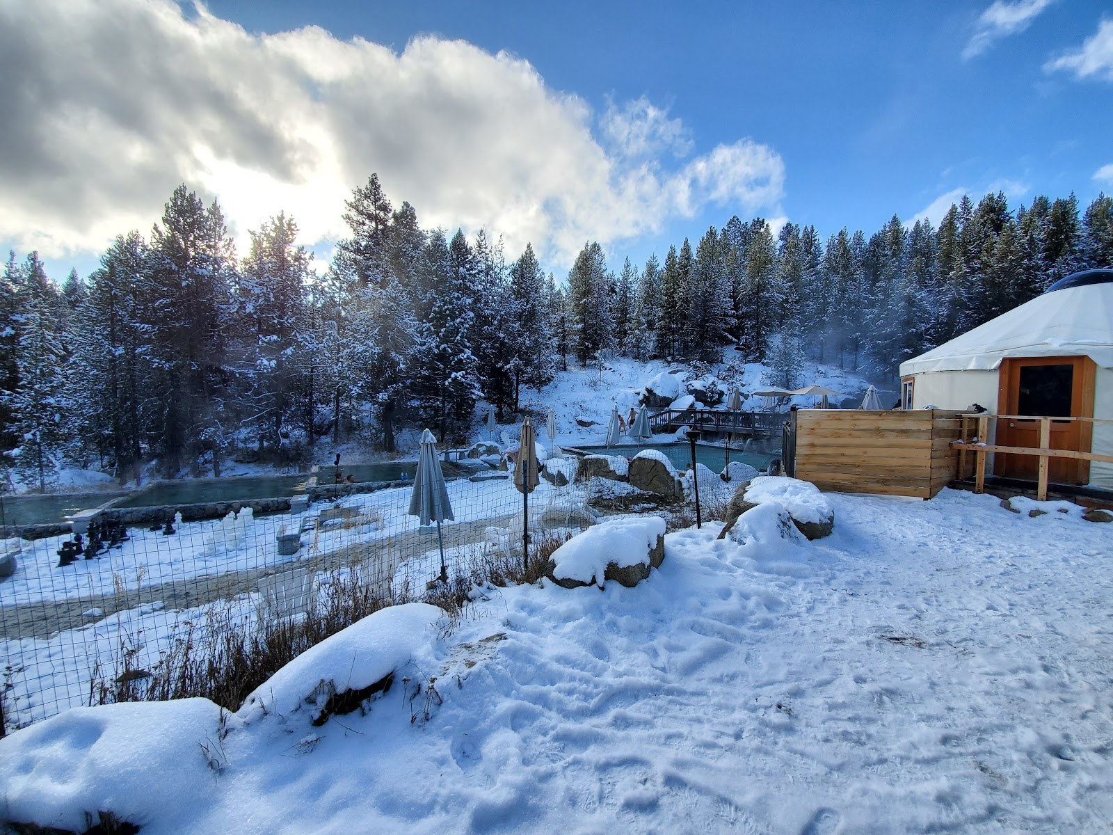 Snow-covered scene of outdoor hot spring pools at Gold Fork Hot Springs near Donnelly, Idaho, with wooden yurt and pine trees in winter