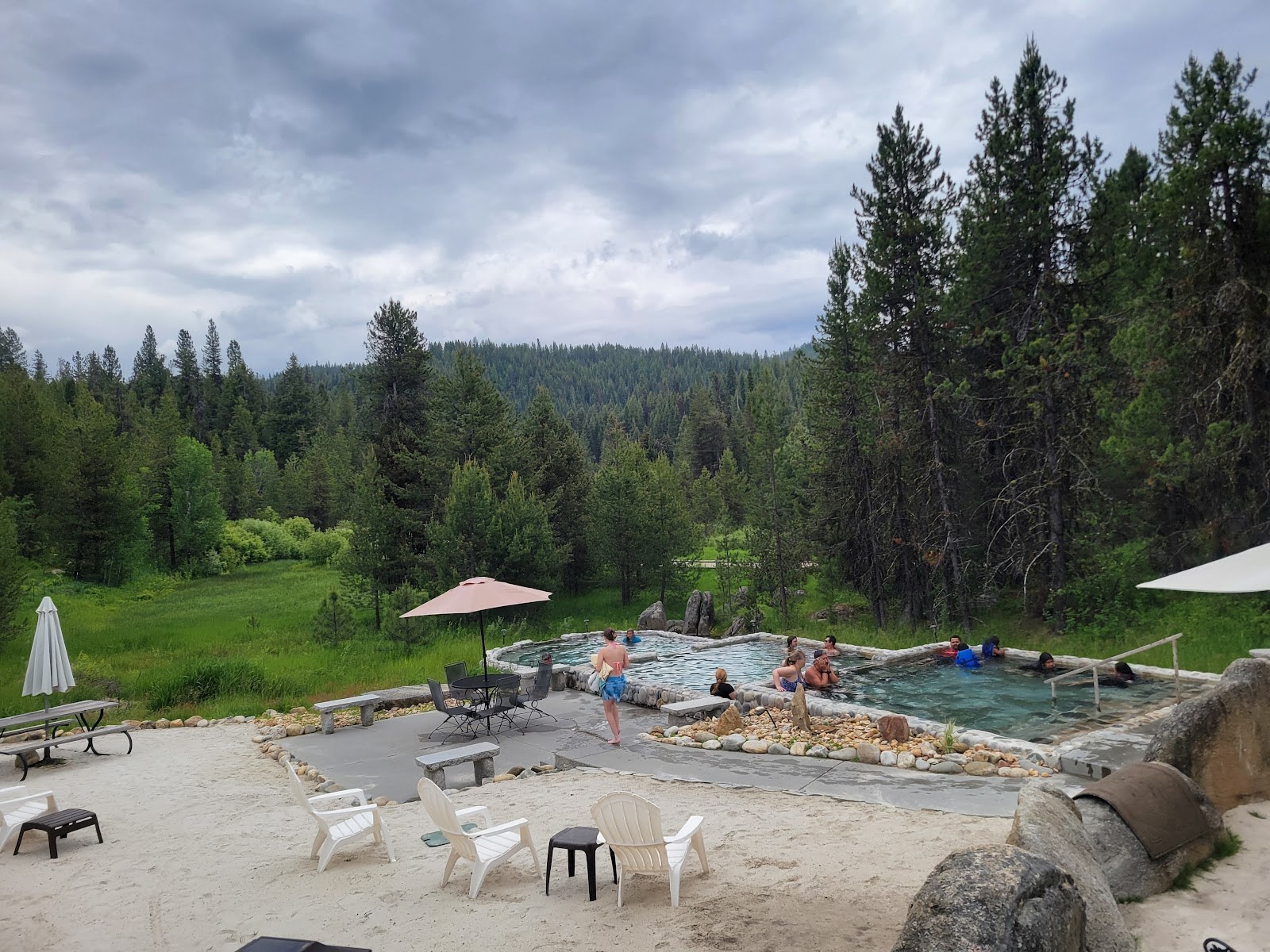 Guests enjoying steaming outdoor hot spring pools at Gold Fork Hot Springs in Donnelly, Idaho, surrounded by lush forest and cloudy sky