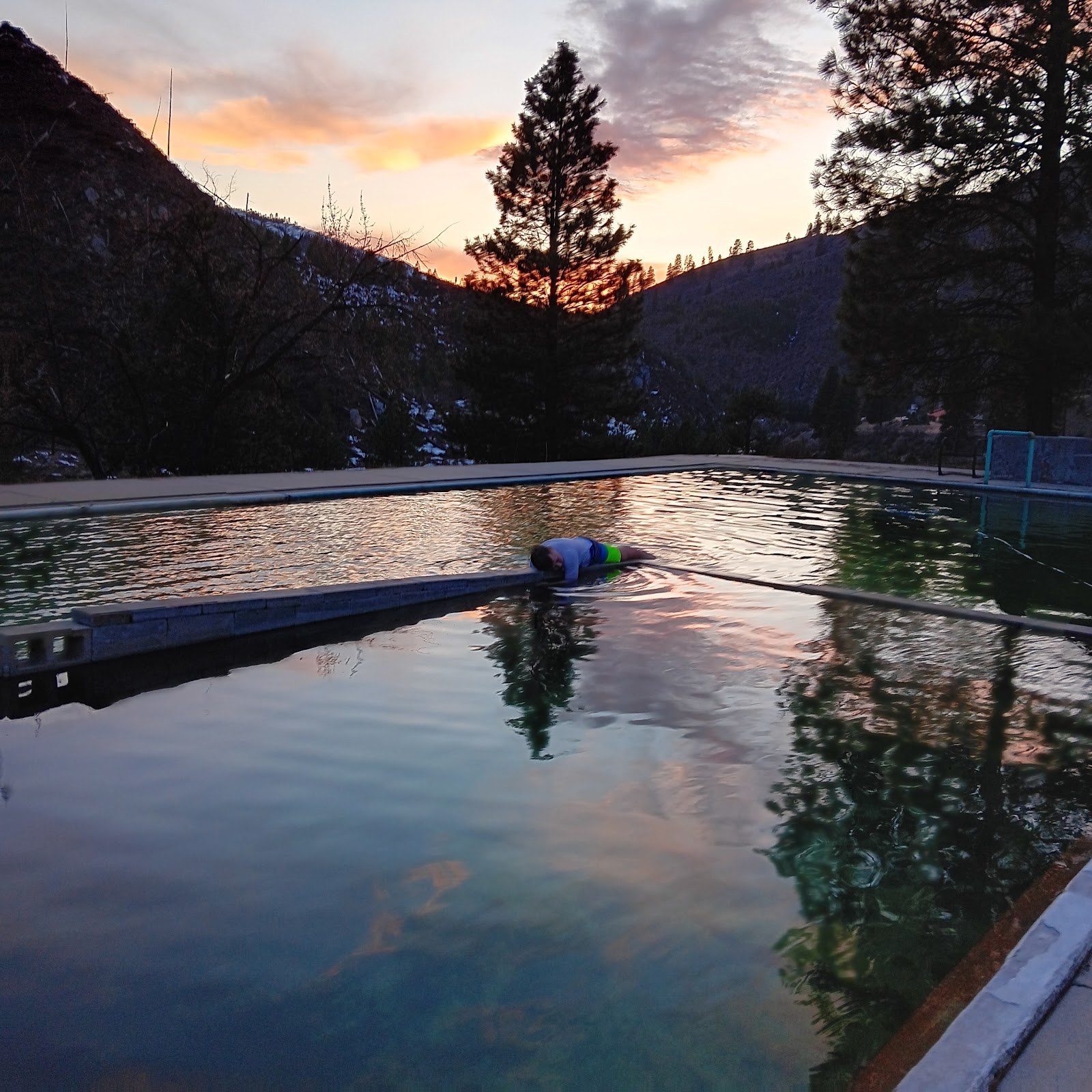 Haven Hot Springs pool reflecting colorful sunset sky, nestled in a forested valley near Lowman, Idaho, during calm evening hours.