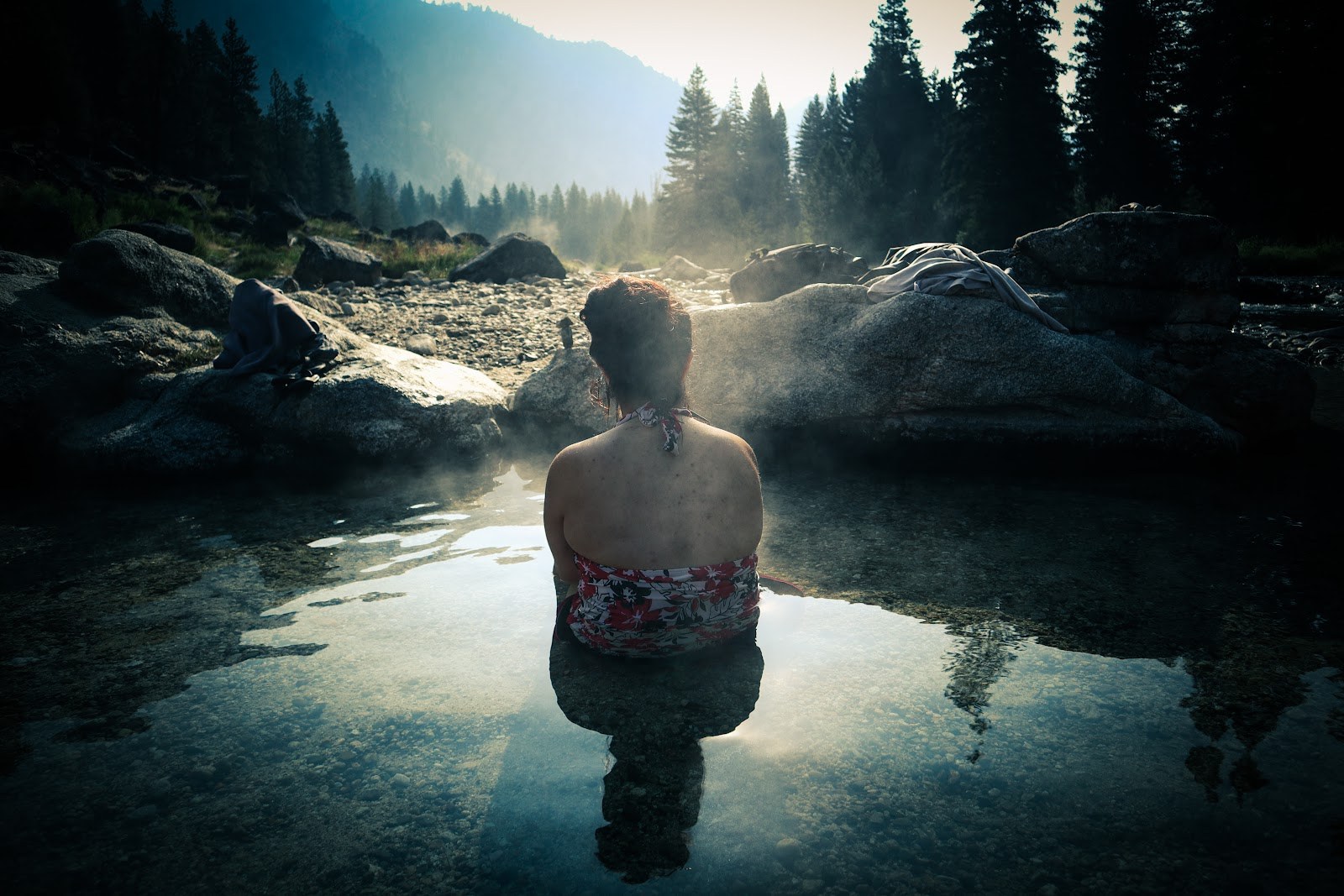 Person soaking in the warm waters of Sacajawea Hot Springs surrounded by rocks and pine trees near Lowman, Idaho, USA