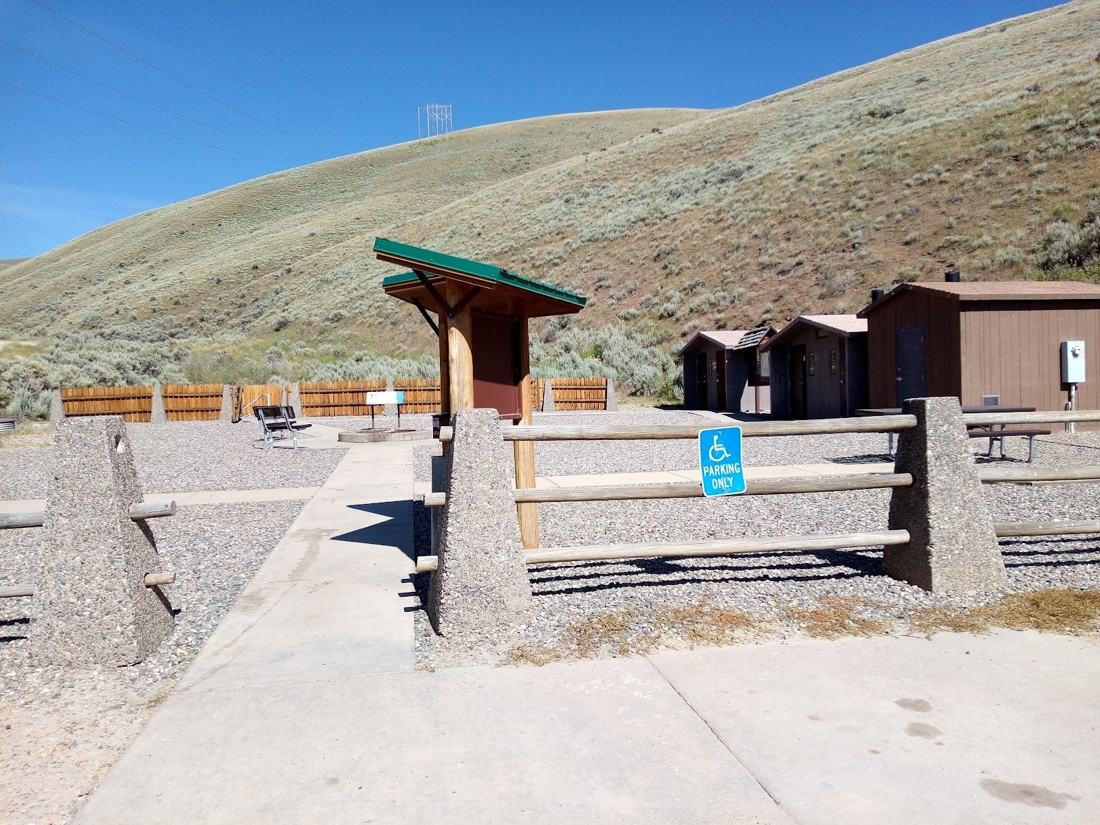 Entrance area to Sharkey Hot Springs near Salmon, Idaho, showing paved path, fencing, and buildings with a backdrop of hills