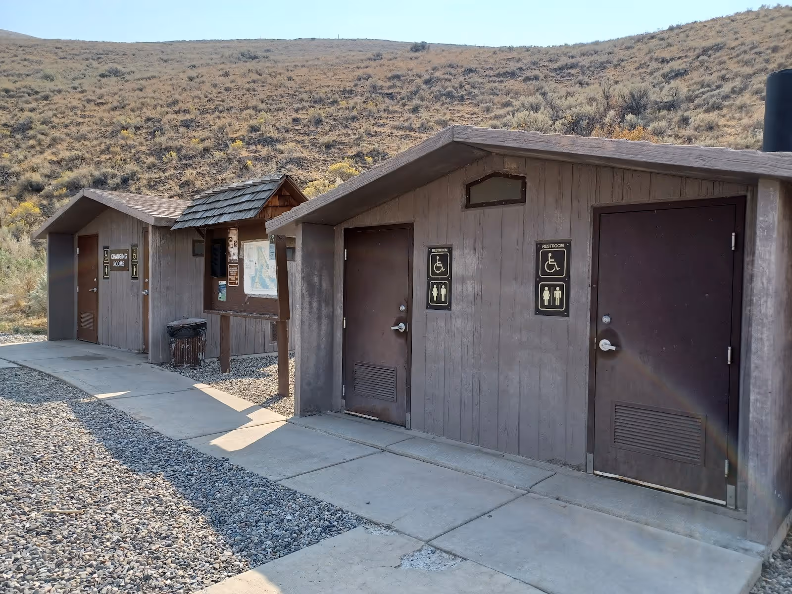 Restroom and changing facilities at Sharkey Hot Springs, Idaho, with signage for accessibility and shaded hillside in the background