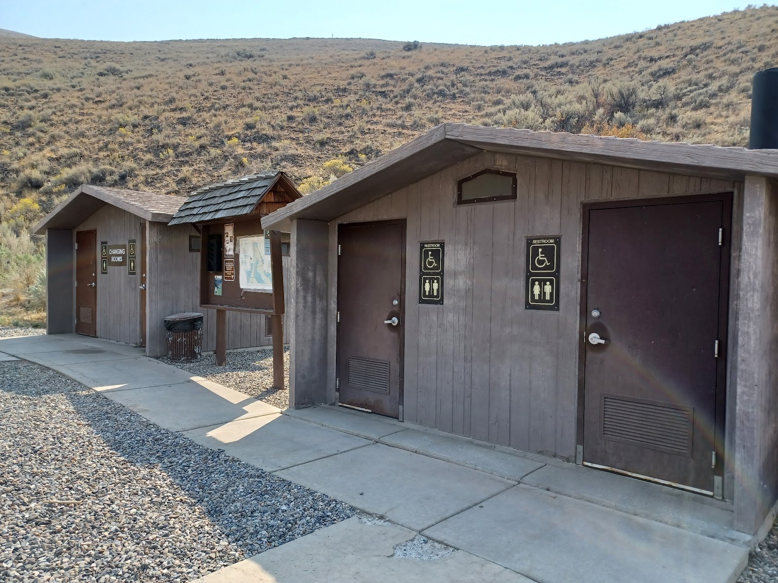 Restroom and changing facilities at Sharkey Hot Springs, Idaho, with signage for accessibility and shaded hillside in the background