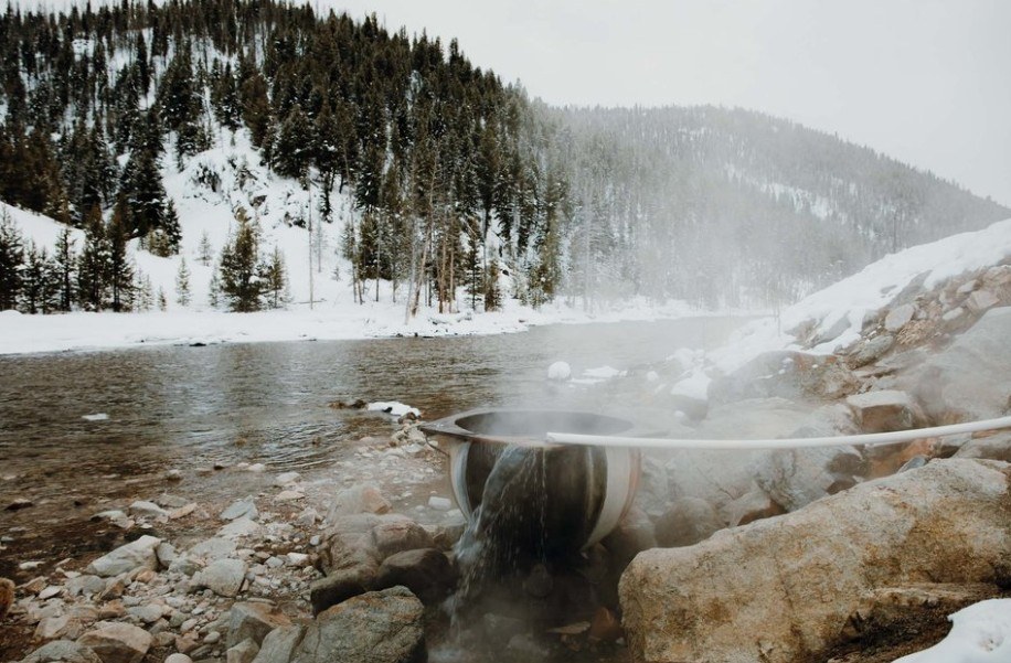 A steamy hot spring pool surrounded by snow-covered rocks and pine trees at Sunbeam Hot Springs, Stanley, Idaho, USA.